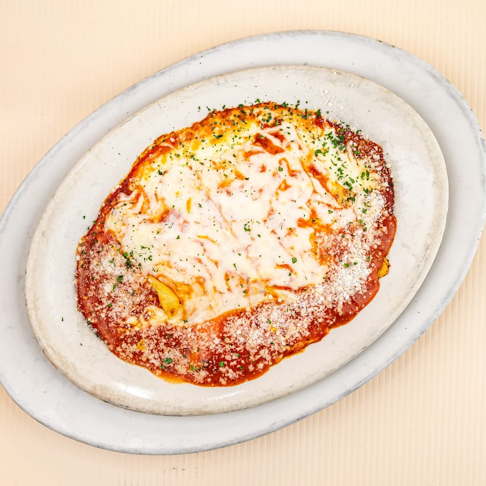 Baked ziti with melted mozzarella, red sauce, parmesan, and parsley in an oval dish.