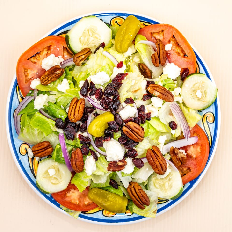 A colorful salad with lettuce, tomatoes, cucumbers, pecans, cranberries, feta, and pepperoncini.