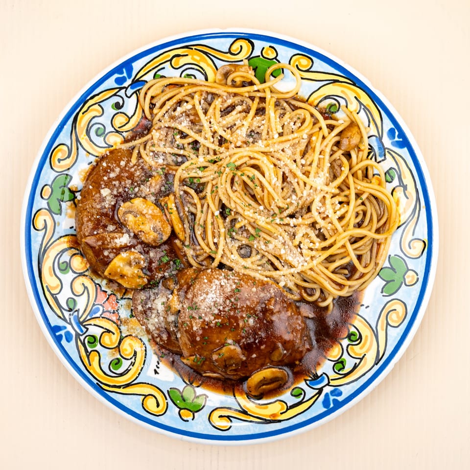 Two large meatballs with mushrooms and gravy, alongside spaghetti, on a colorful plate.