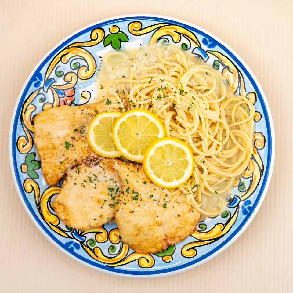 Chicken piccata with spaghetti, lemon slices, and parsley on a colorful Italian-style plate.