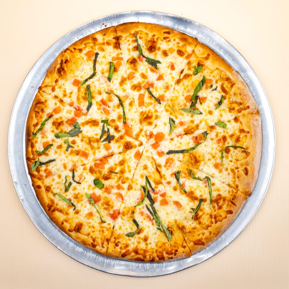 All Star Pizza's sliced Margherita pizza with mozzarella, diced tomatoes, and fresh basil on a metal pan.