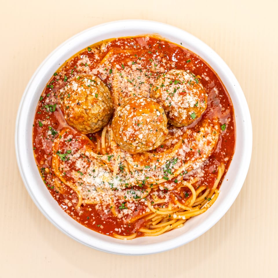 Spaghetti and meatballs in a white bowl, topped with red sauce, parmesan, and parsley.