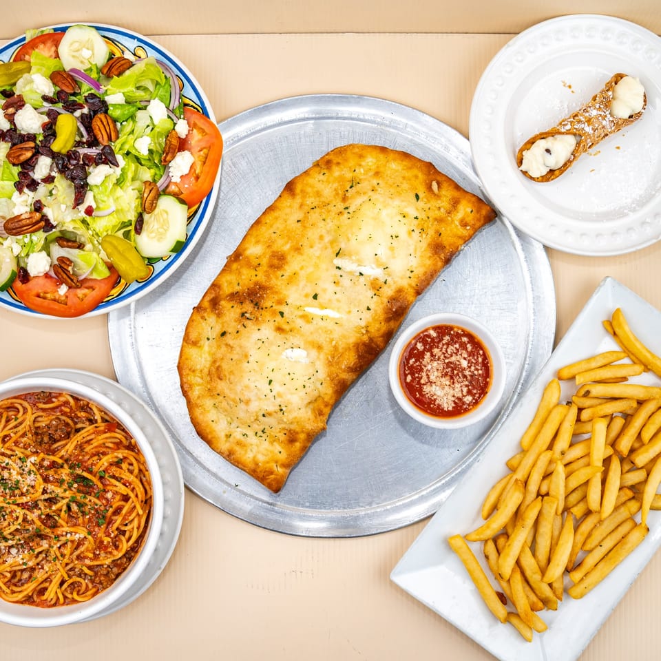 Overhead view of a calzone, spaghetti, salad, fries, and cannoli from All Star Pizza & Italian Restaurant.